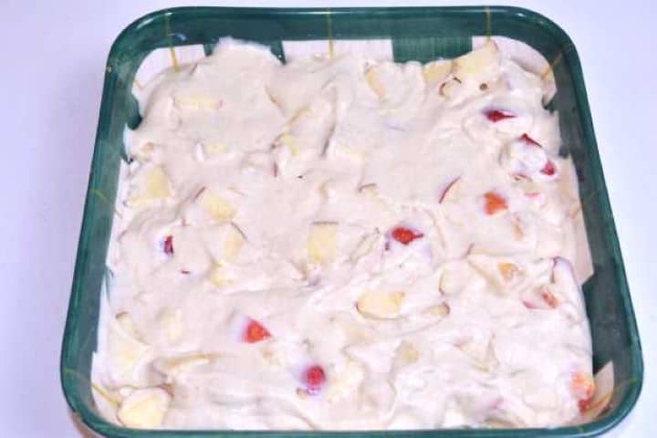 Apple cake batter spread evenly in a greased ceramic square baking dish ready for the oven.