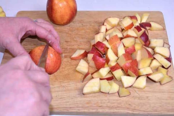 Fresh unpeeled apples cored and cut into hearty one-inch cubes on a wooden cutting board.