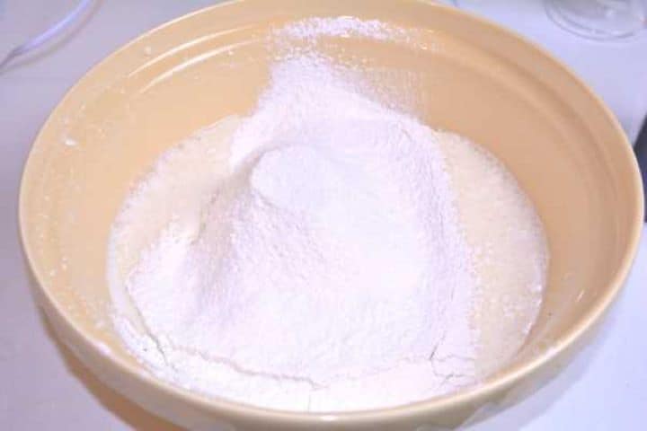 Sifting plain flour and baking powder over the wet batter in a mixing bowl.