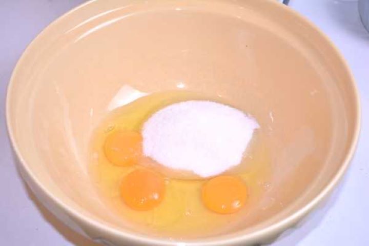 Three eggs, caster sugar, and salt in a glass mixing bowl ready to be beaten until pale and foamy.
