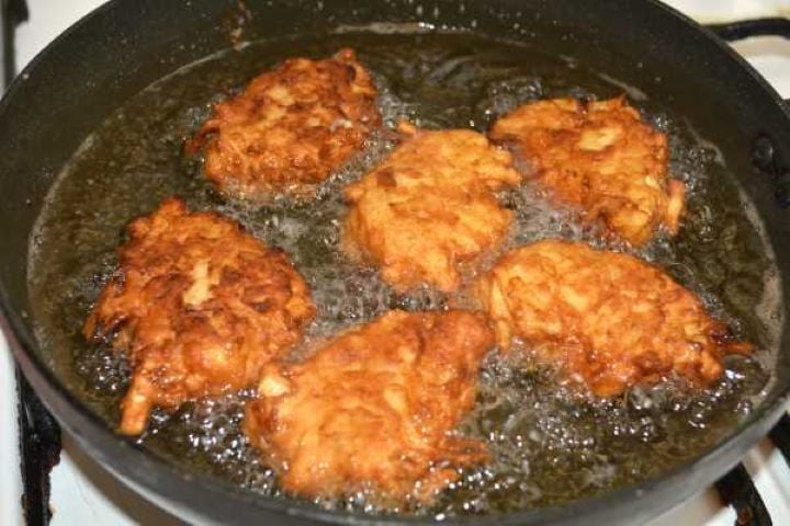 Golden-brown crispy grated apple fritters being flipped in a skillet to fry the other side.