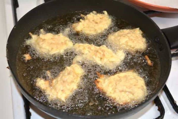 Spoonfuls of grated apple drop-batter shallow frying in hot sunflower oil in a skillet.
