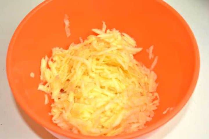 Freshly grated apples tossed with lemon juice in a bowl to preserve color and natural juices.