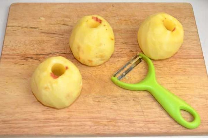 Peeled and cored apples on a wooden cutting board ready to be coarsely grated for fritters.