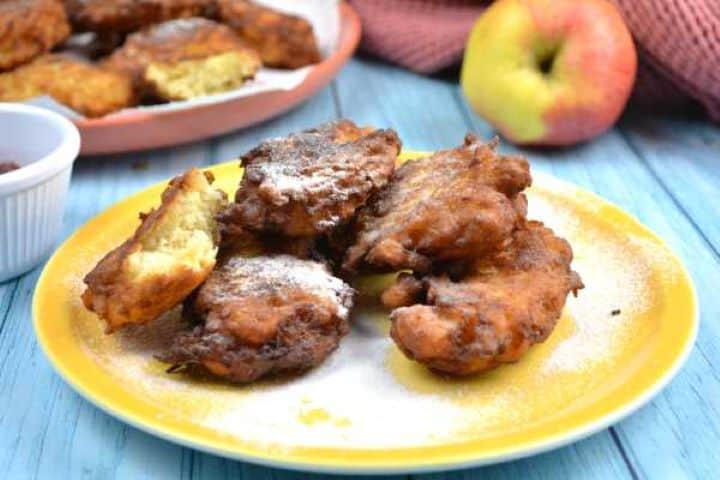 Stack of homemade grated apple fritters generously dusted with powdered sugar on a yellow plate.