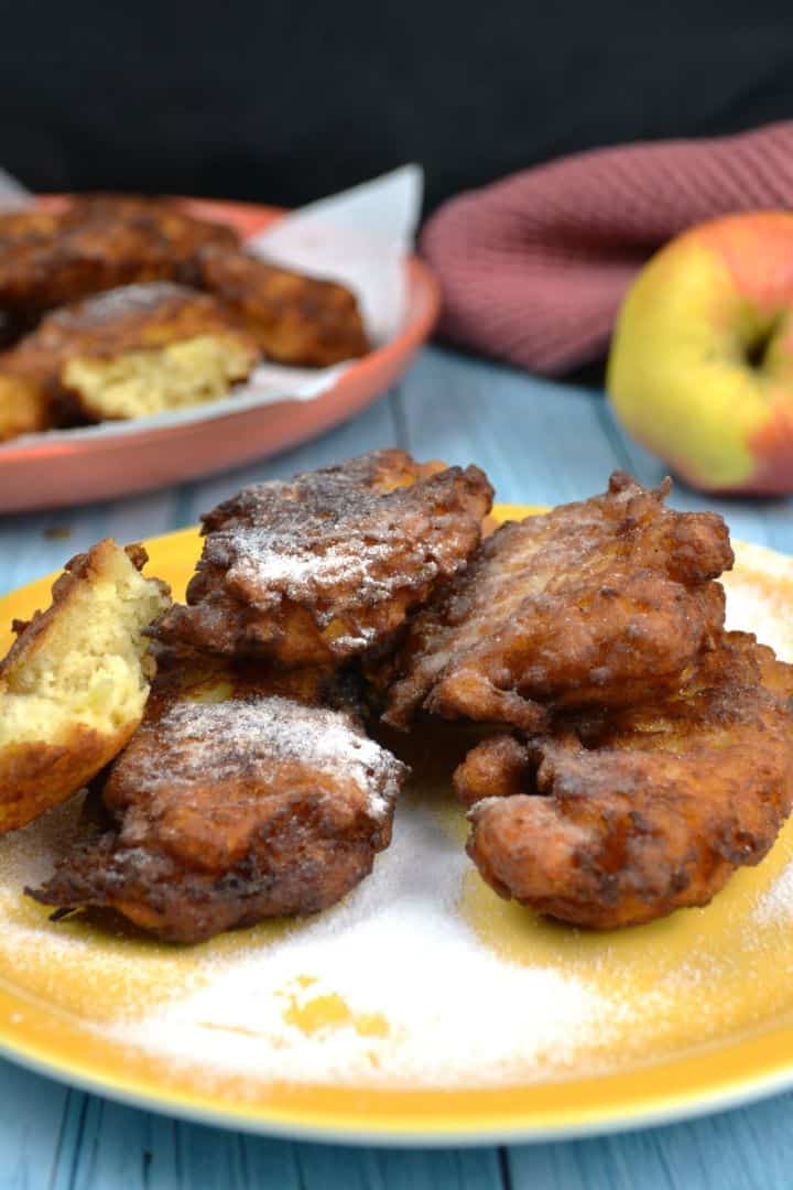 Crispy golden grated apple fritters served warm on a plate with strawberry jam and a dusting of sugar.
