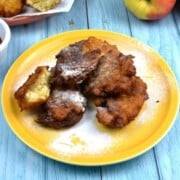 Crispy golden grated apple fritters served warm on a plate with strawberry jam and a dusting of sugar.