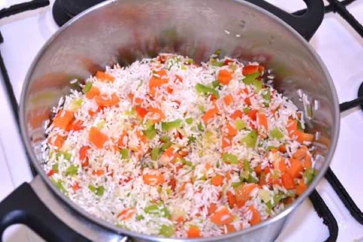 Stirring long-grain white rice into a pot of sautéed leeks and bell peppers to toast the grains before adding liquid.