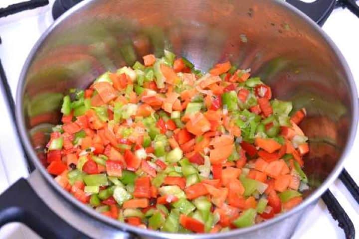 Sautéing thinly sliced sweet leeks, diced carrots, and peppers in a pot with sunflower oil.