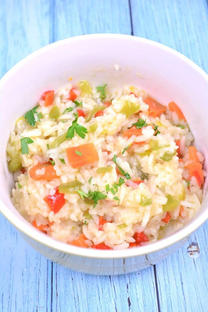 A white ceramic bowl filled with fluffy vegetable rice pilaf featuring vibrant red and green bell peppers, sweet leeks, and diced carrots.