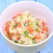 A white ceramic bowl filled with fluffy vegetable rice pilaf featuring vibrant red and green bell peppers, sweet leeks, and diced carrots.