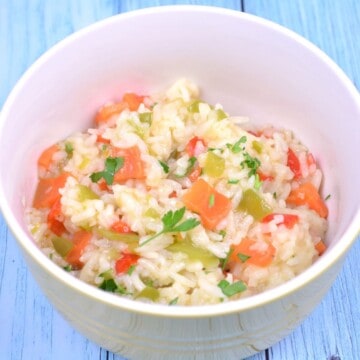 A white ceramic bowl filled with fluffy vegetable rice pilaf featuring vibrant red and green bell peppers, sweet leeks, and diced carrots.