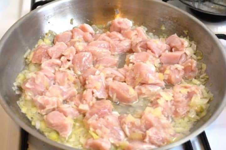 Adding diced turkey breast meat to the sautéed onions in the frying pan.