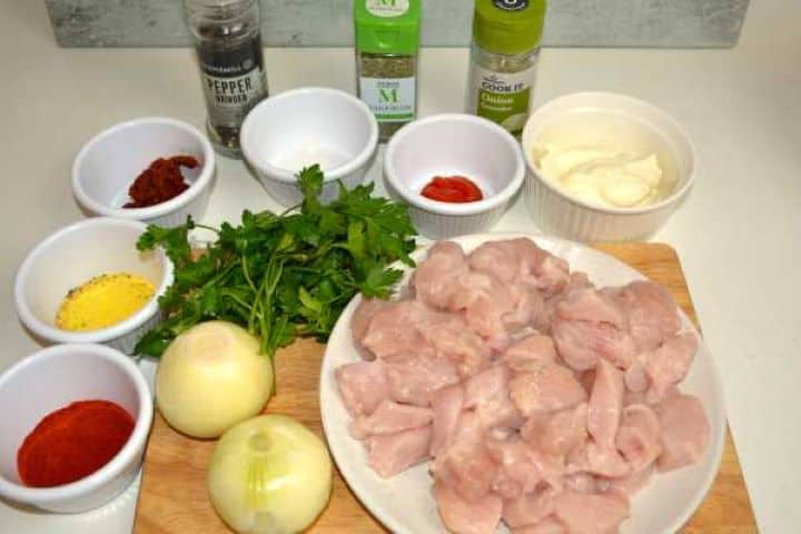 Ingredients for the turkey paprikash: diced turkey breast, chopped onions, fresh parsley, and Hungarian sweet paprika powder on a wooden chopping board.