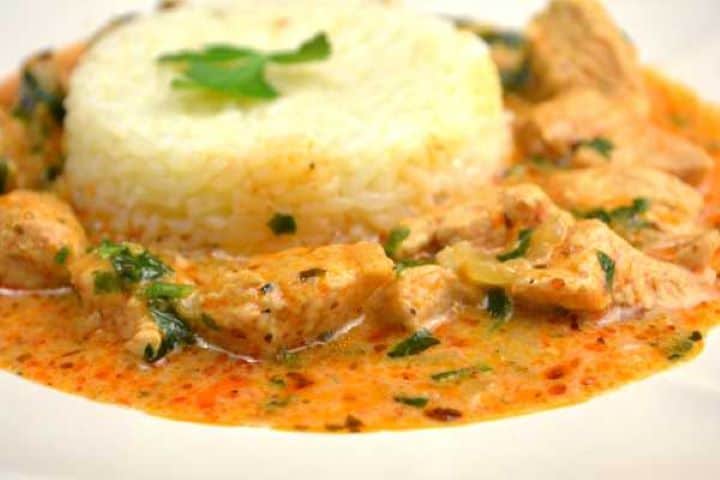 A close-up of a serving of Hungarian turkey paprikash with a silky paprika sauce over fluffy white rice.
