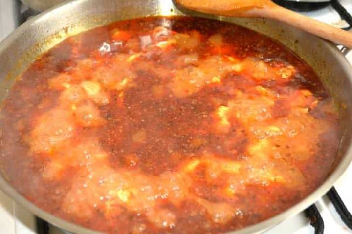 The turkey paprikash gently simmering in the pan with water, creating a fragrant red broth.