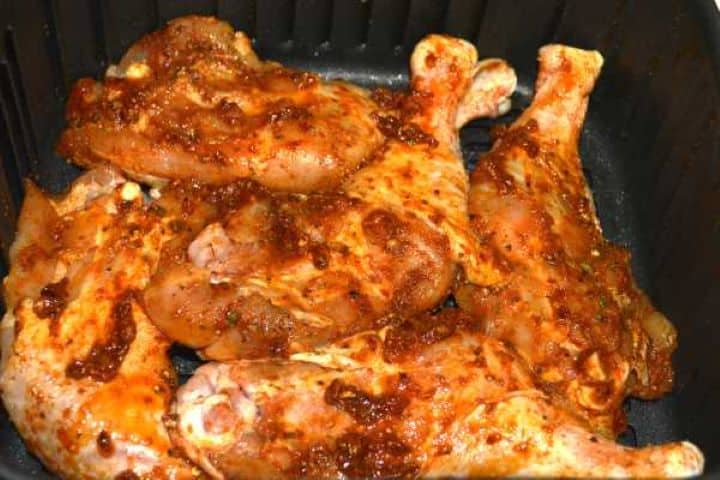 before frying Marinated whole chicken legs placed skin-side down in a single layer inside a Cosori air fryer basket before cooking.