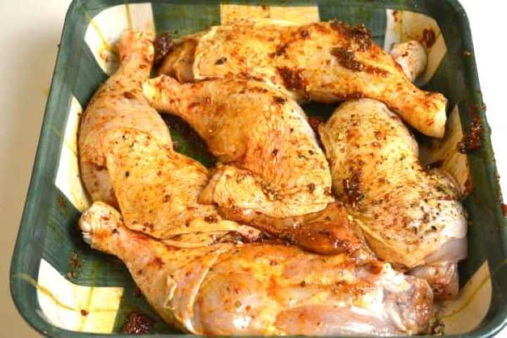 seasoned Bone-in skin-on chicken leg quarters thoroughly coated in a red paprika and coriander marinade resting in a bowl.