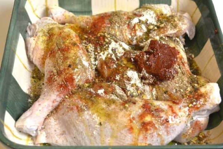 seasoning Raw whole chicken leg quarters arranged in a bowl next to olive oil, Hungarian paprika, and pepper paste marinade ingredients.