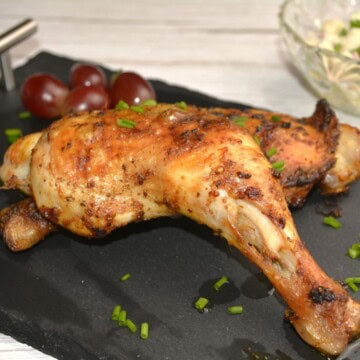 Two crispy air fryer whole chicken legs served skin-side up on a black slate platter with fresh grapes.