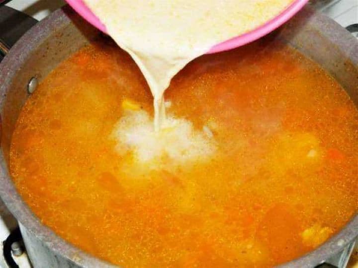 Pouring the tempered sour cream liaison into a golden pot of Greek style lemon chicken soup with rice and shredded chicken.