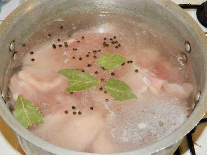 Simmering chicken pieces with whole onion, carrots, parsnip, and bay leaves in a large pot of water to make clear broth.