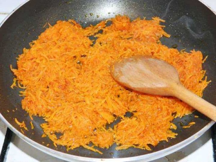 Sautéing finely grated carrots in olive oil in a skillet to create a vibrant golden color base for the chicken soup.