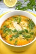 A yellow bowl filled with creamy Greek style lemon chicken soup with sour cream, garnished with fresh parsley.
