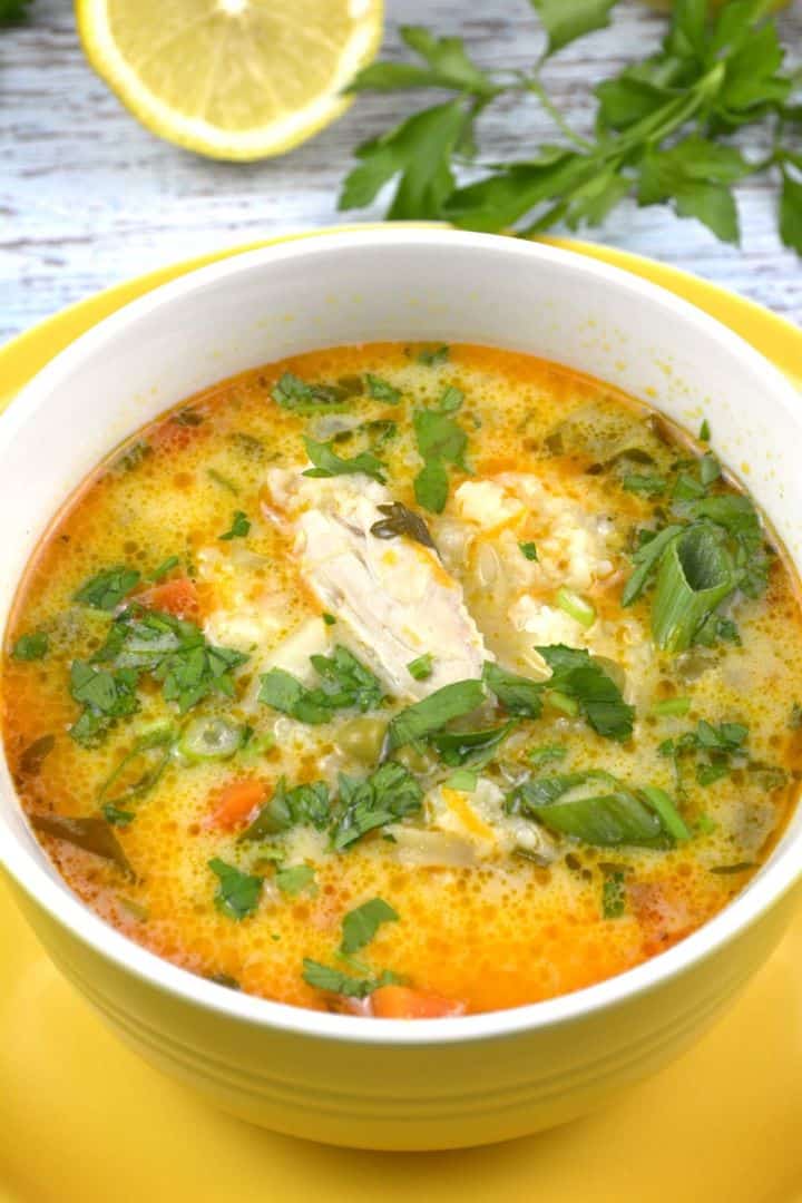 serving A yellow bowl filled with creamy Greek style lemon chicken soup with sour cream, garnished with fresh parsley.