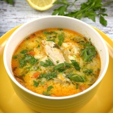 A yellow bowl filled with creamy Greek style lemon chicken soup with sour cream, garnished with fresh parsley.