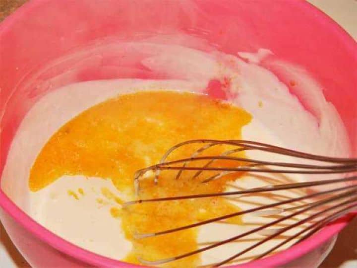 Whisking hot chicken broth into a bowl of sour cream and egg yolks to temper the mixture and prevent curdling.