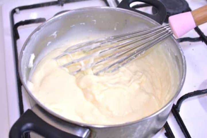 Whisking melted cheddar into a smooth, glossy stovetop cream cheese mixture.