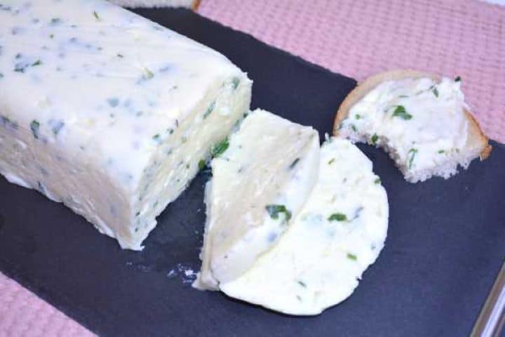 serve Sliceable homemade herb cheese block cut into thick pieces on a serving platter with bread slices.