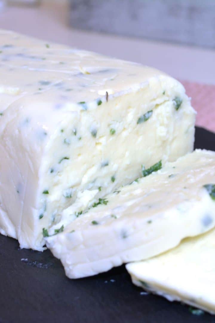 Slices of homemade herbed cream cheese served on a black tray with fresh crusty bread.