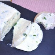 Slices of homemade herbed cream cheese served on a black tray with fresh crusty bread.