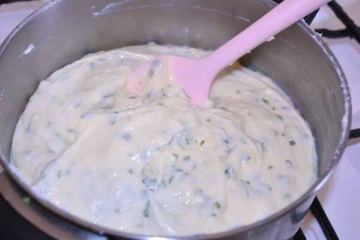 seasoned Stirring fresh green herbs evenly into the warm homemade cheese spread in a saucepan.