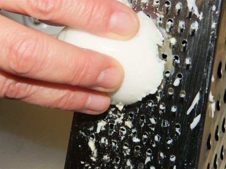 Grating the eggs Finely grating peeled hard-boiled eggs using a metal box grater into a glass mixing bowl to make a smooth egg salad without mayo.