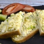 Creamy Hungarian egg salad spread smoothly onto sliced crusty sourdough bread with tomato and garnished with fresh chopped chives.