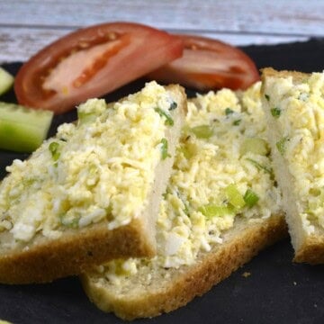 Creamy Hungarian egg salad spread smoothly onto sliced crusty sourdough bread with tomato and garnished with fresh chopped chives.