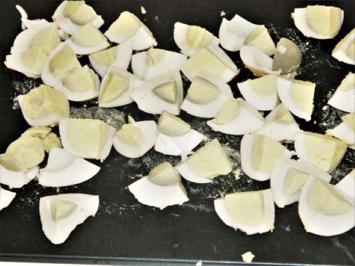 Cutting peeled hard-boiled eggs into bite-sized pieces on a cutting board.