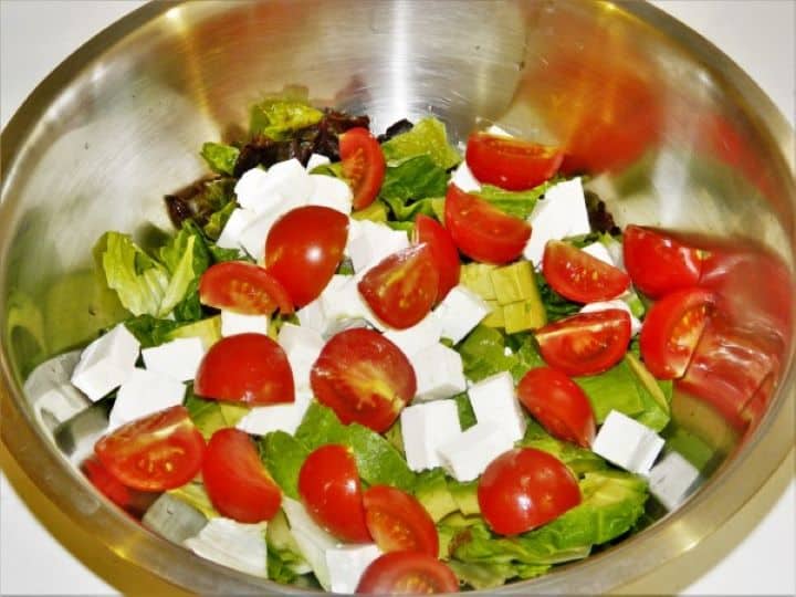 Halved cherry tomatoes added to the salad bowl with avocado, lettuce, and feta.