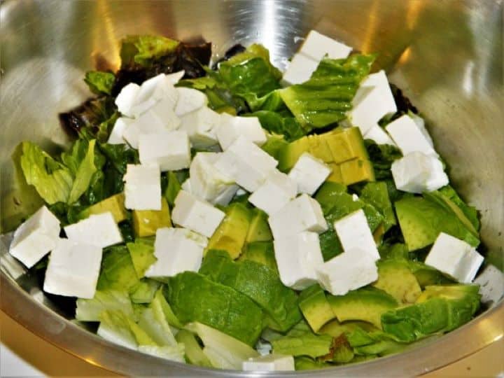 Cubed Greek feta cheese added to the bowl with romaine lettuce and sliced avocado.