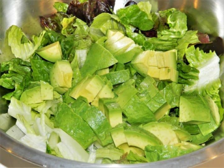 Sliced ripe avocado arranged over chopped romaine lettuce in a salad bowl.
