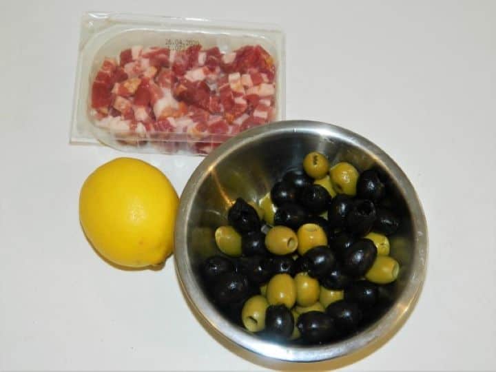 Salad prep ingredients including green and black pitted olives, fresh lemon, and chopped smoked bacon.