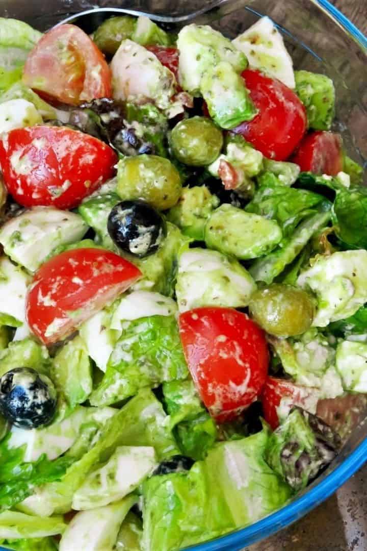 Loaded tomato avocado egg salad served in a glass bowl with crispy bacon, feta, and olives.