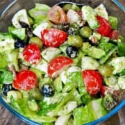 Loaded tomato avocado egg salad served in a glass bowl with crispy bacon, feta, and olives.