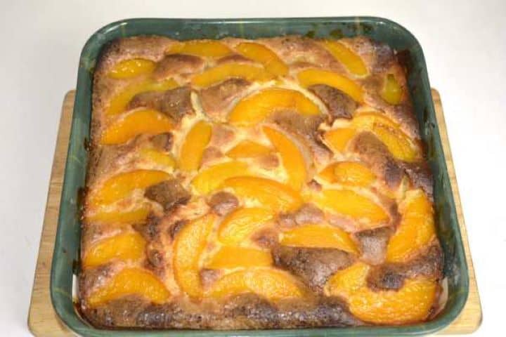 Golden brown old fashioned peach cake with canned peaches dusted with powdered sugar in a ceramic pan.