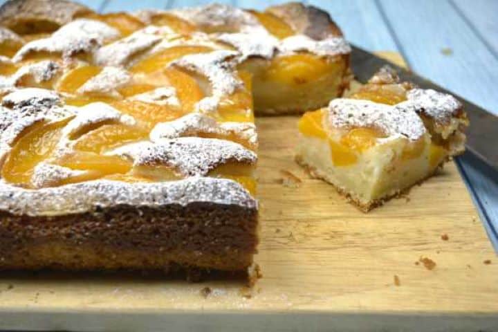 A close-up shot of a single slice of moist Transylvanian yogurt peach cake showing the light, fluffy sponge texture on the wooden cutting board.