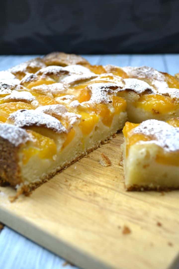 Slices of old fashioned Transylvanian peach cake with canned peaches served on a wooden cutting board.