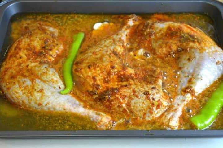 Pouring a bottle of beer into a roasting pan around seasoned turkey legs and fresh vegetables for an oven-braised recipe.